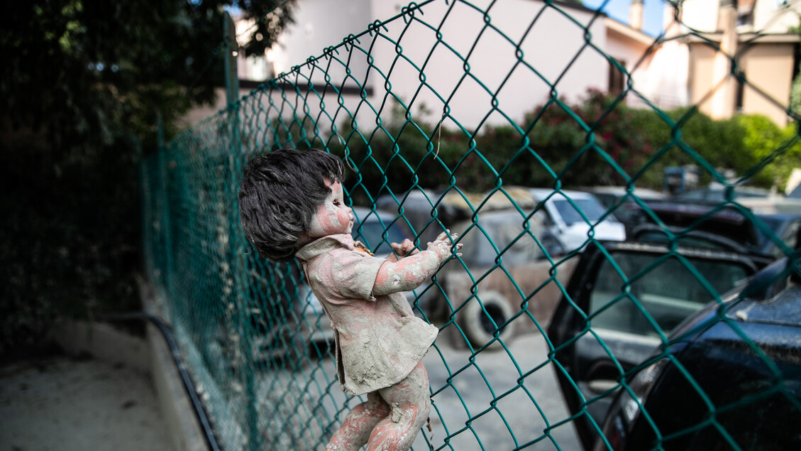 Una bambola incastrata nella rete di un 'area per i giochi dei bambini ricoperta del fango dell 'alluvione di un mese fa, Faenza (Ravenna) - RIPRODUZIONE RISERVATA