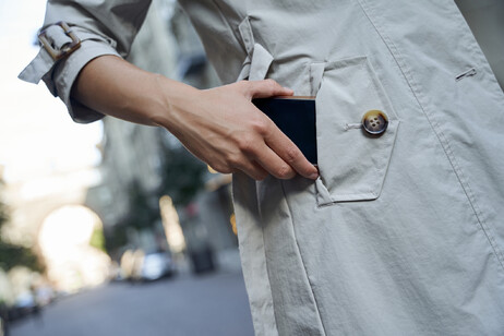 Una donna mette nella tasca del trench uno smartphone foto iStock.