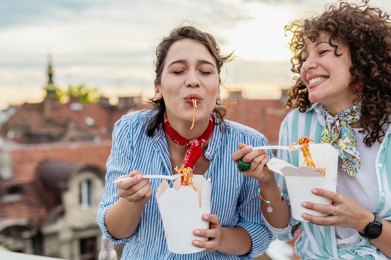 Due donne sorridenti mangiano pasta come street food foto iStock. -     RIPRODUZIONE RISERVATA